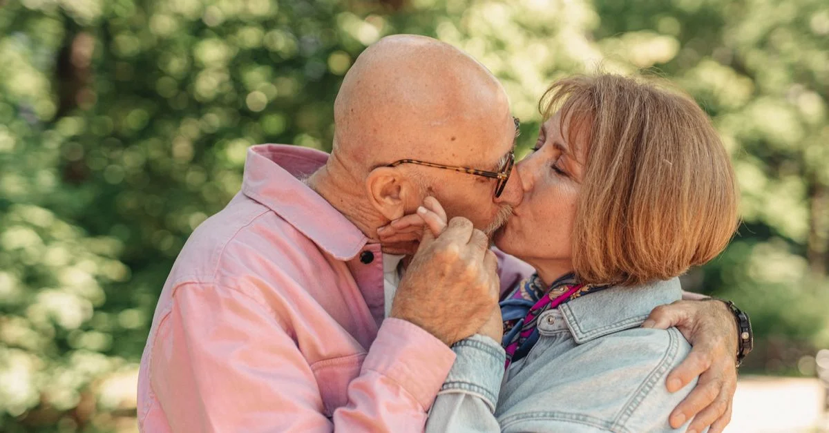 Un couple senior partage un tendre baiser en extérieur, capturant un moment d'amour et de connexion.