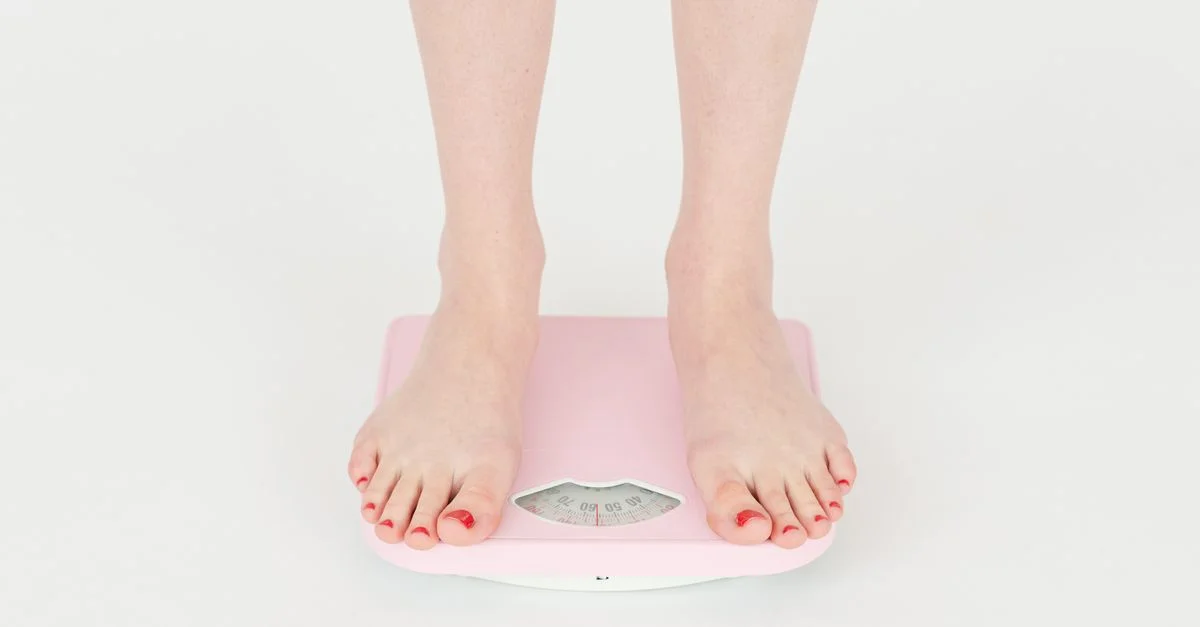 Gros plan sur les pieds d'une femme sur une balance rose, axé sur la gestion du poids.