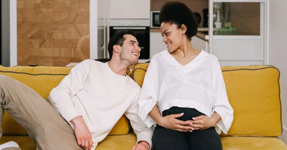 Couple joyeux et attendu se relaxant chez eux sur un canapé jaune vibrant, partageant un moment d'amour.