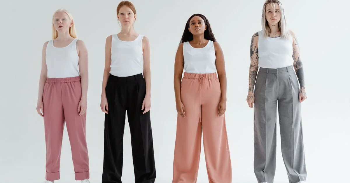 Quatre femmes diverses se tiennent confiantes dans des pantalons élégants et des débardeurs blancs devant un fond blanc.