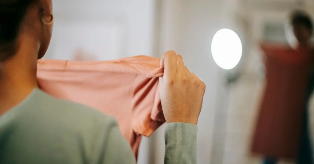 Une femme examine une nouvelle tenue rose devant un miroir, capturant le mode de vie moderne et la mode.