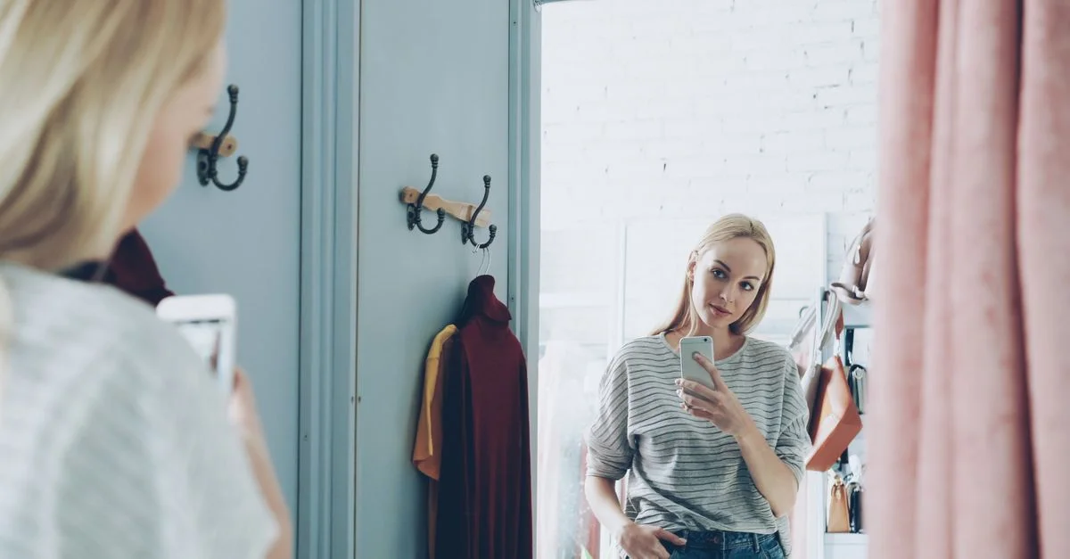 Femme à la mode prend un selfie dans un cadre élégant de cabine d'essayage, capturant son reflet.