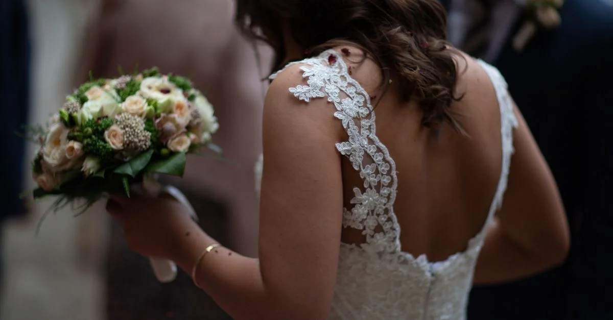 Une mariée en robe en dentelle tient un magnifique bouquet, vue de derrière lors d'une cérémonie de mariage.