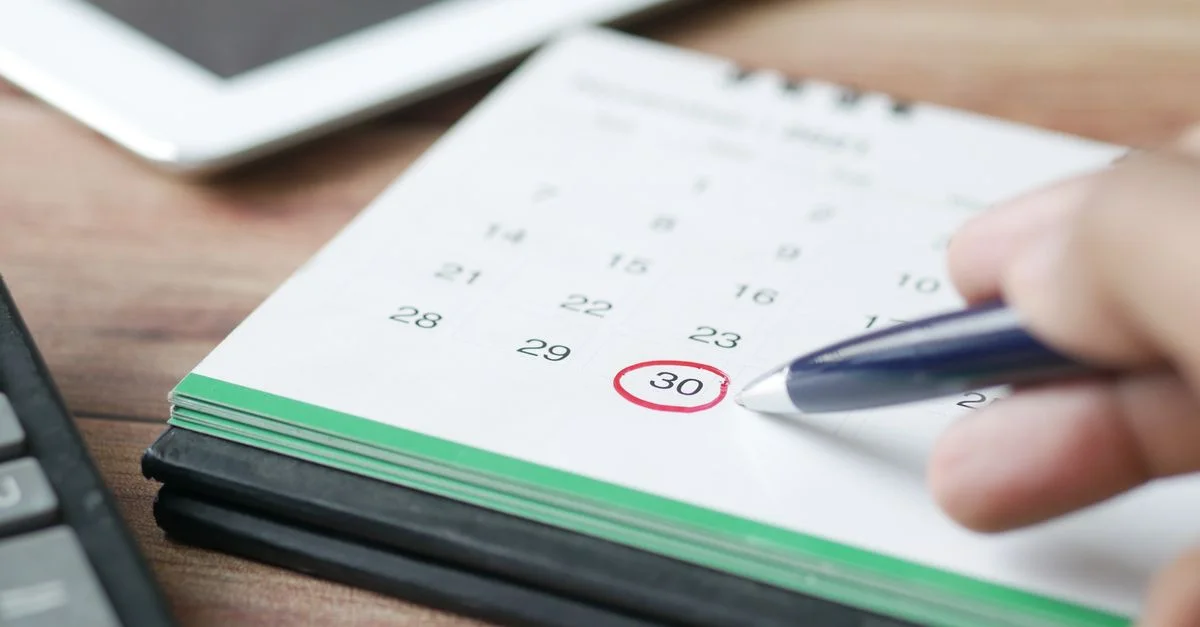 Gros plan d'une main marquant une date sur un calendrier avec un stylo, soulignant la planification et la programmation.