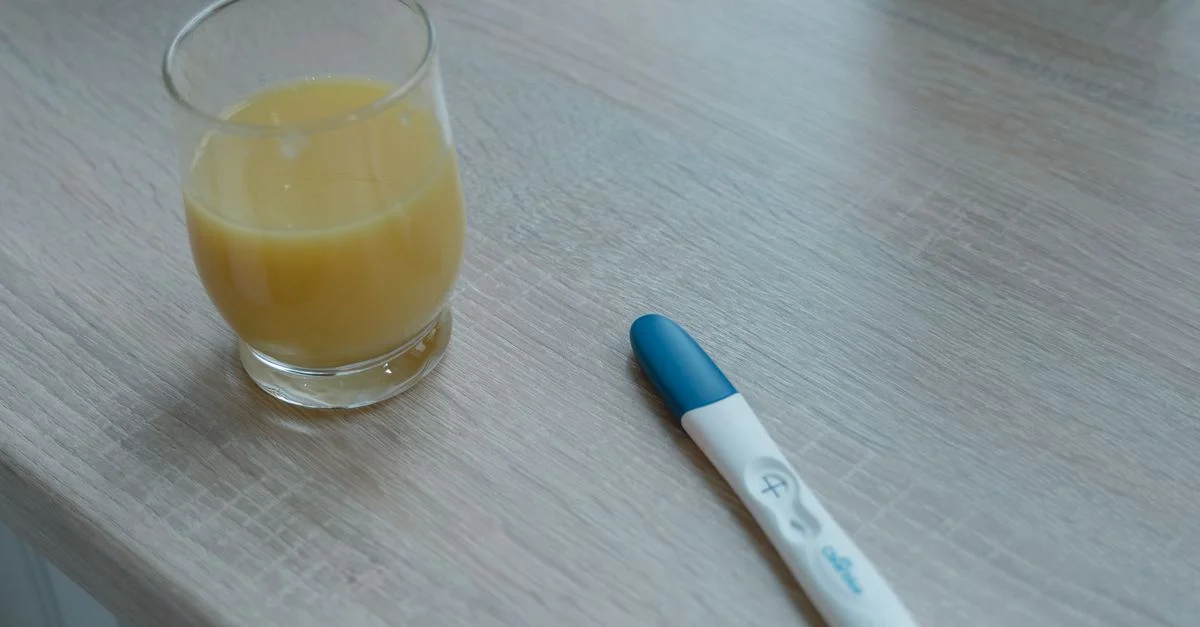 Un verre de jus d'orange et un test de grossesse positif placés sur une table en bois.