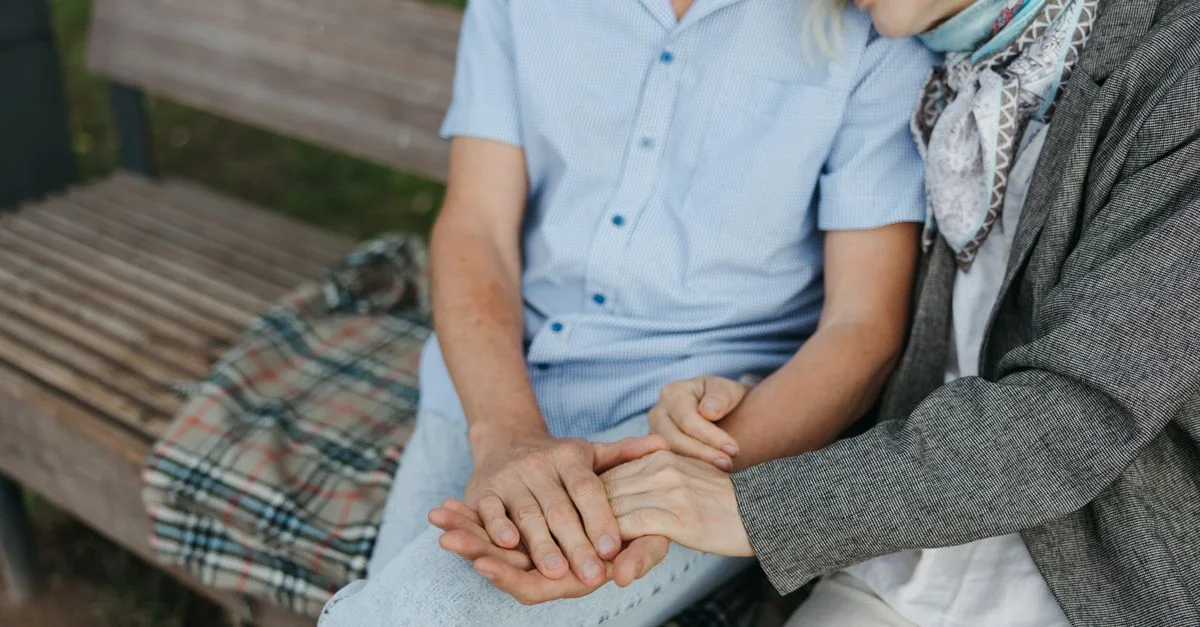 Un moment touchant d'un couple âgé se tenant par la main sur un banc dans un parc, symbolisant l'amour et la compagnie.