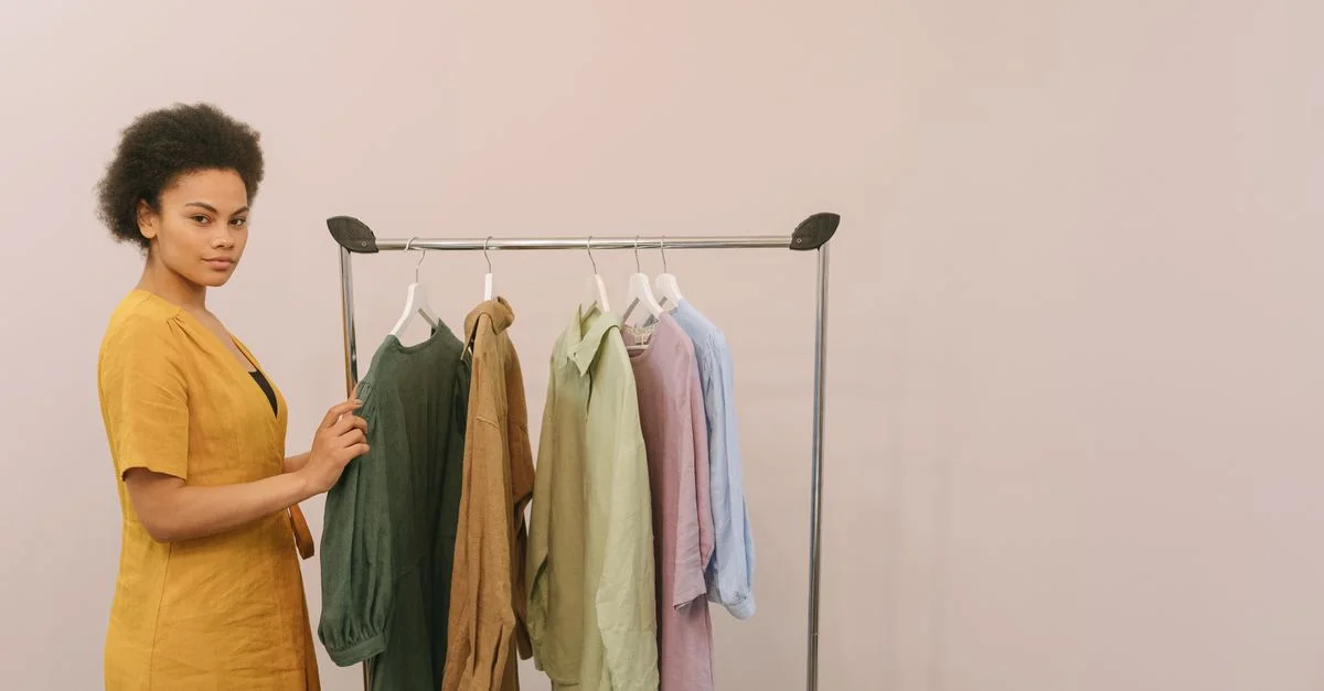 Femme afro-américaine dans une boutique de mode présentant des vêtements colorés sur un portant.