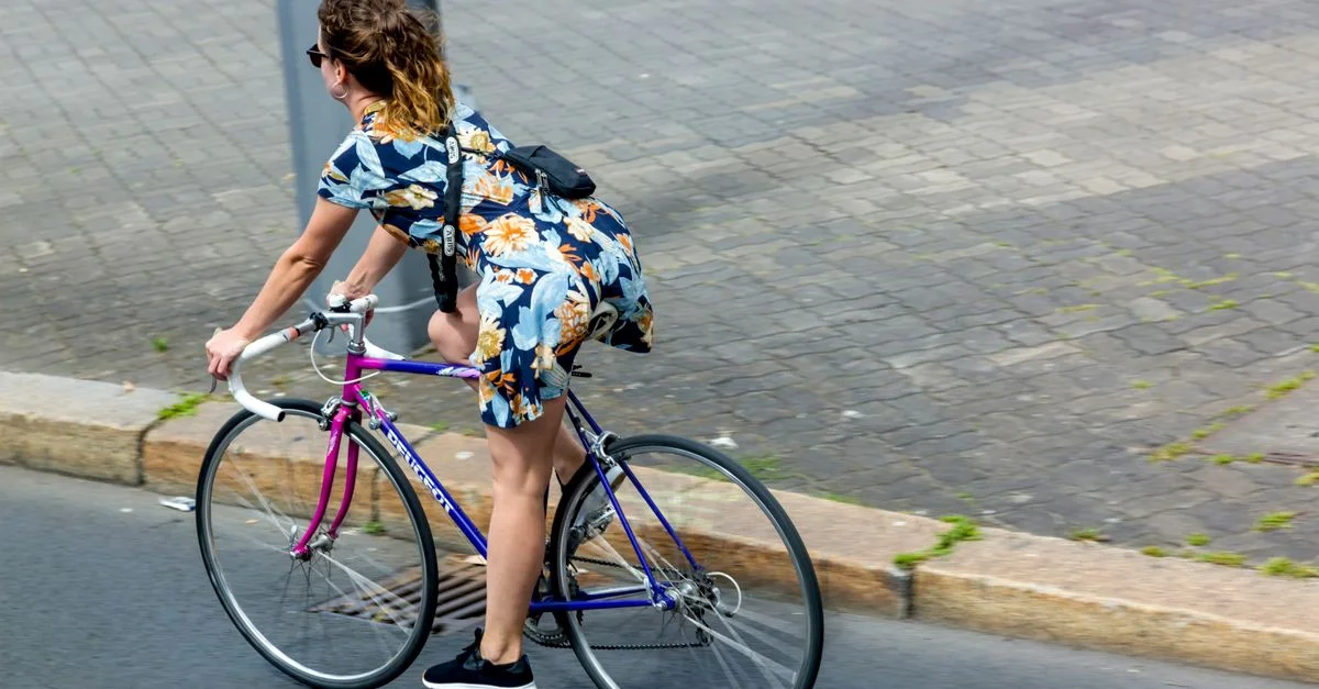 Une femme en robe fleurie fait du vélo dans une rue de la ville, mettant en valeur le style de vie urbain et les voyages.