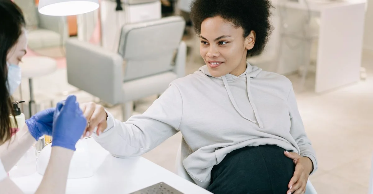 Femme enceinte avec des cheveux afros se faisant une manucure dans un salon de manucure tout en souriant et se relaxant.