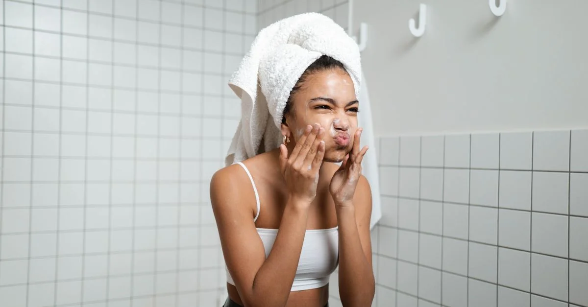 Une jeune femme applique de la crème pour le visage dans une salle de bain moderne, promouvant les soins de la peau et un mode de vie sain.