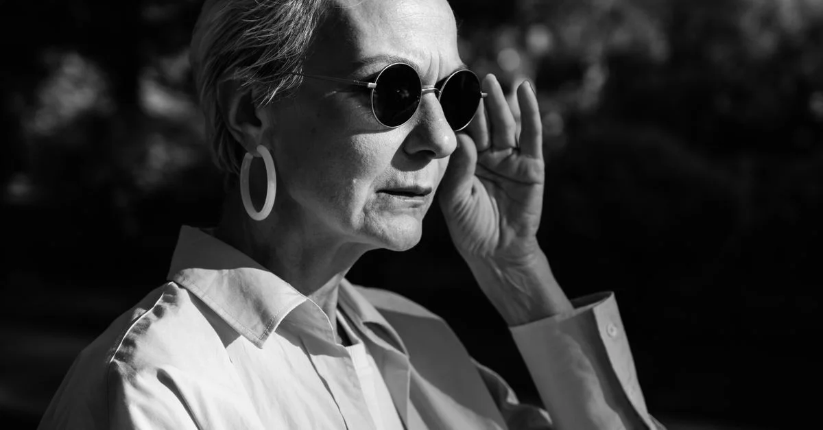 Portrait en noir et blanc d'une femme senior élégante portant des lunettes de soleil en extérieur.