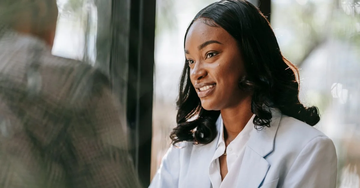 Femme noire professionnelle en tenue de bureau souriante lors d'une réunion à l'intérieur.