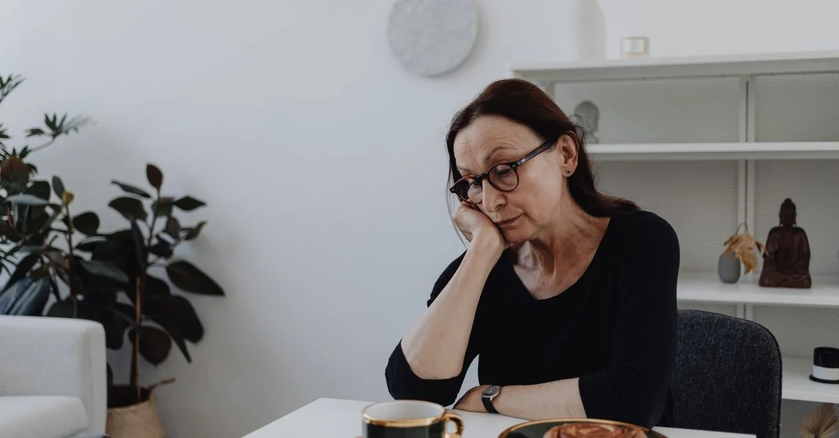 Une femme d'âge moyen pensive est assise à une table avec des pâtisseries et une tasse de café.