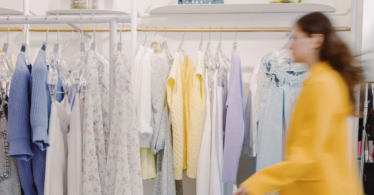 Femme floue passe devant un portant de vêtements colorés dans un magasin de mode intérieur.