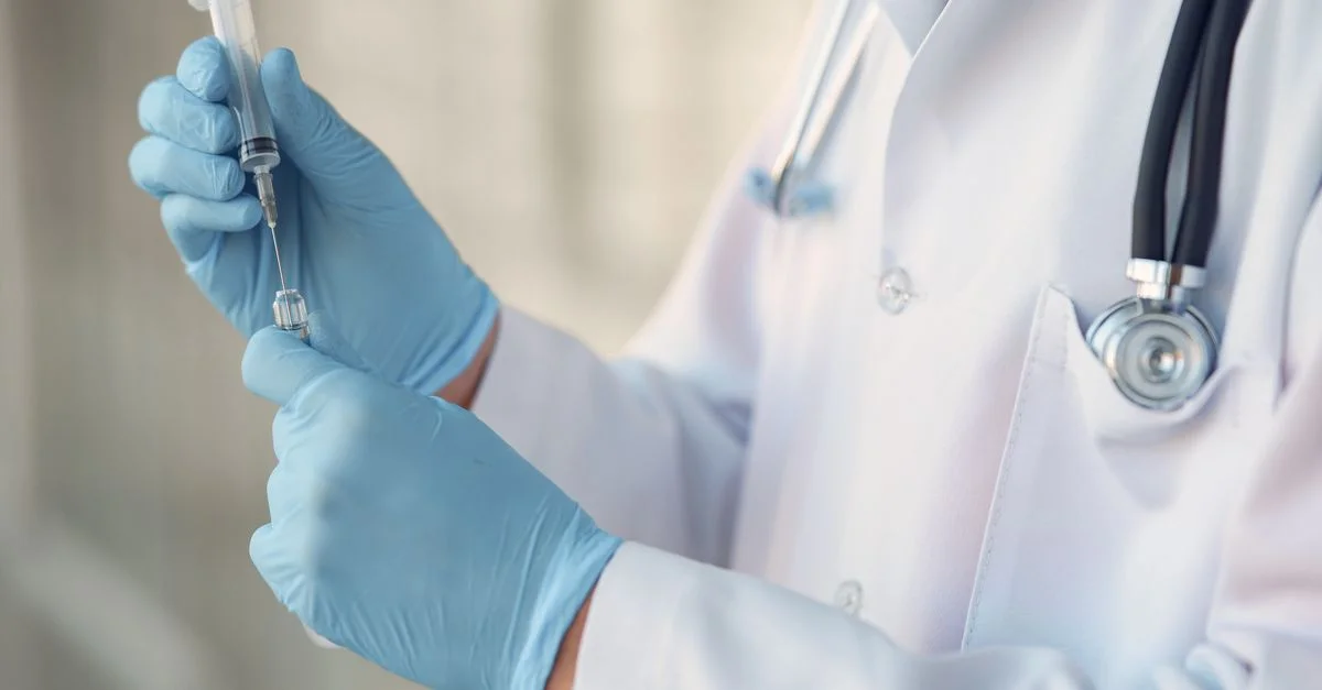 Professionnel de la santé portant des gants et tenant une seringue dans un cadre clinique.