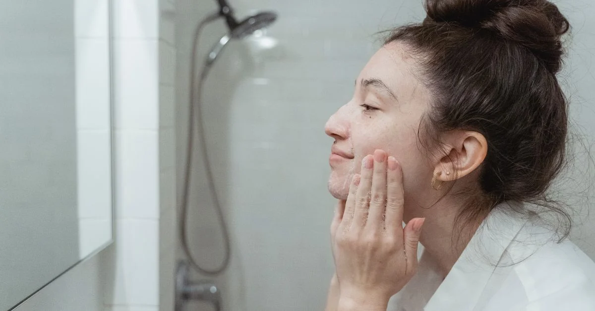 Une femme appliquant de la crème pour le visage devant un miroir dans sa routine de soins de la peau dans une salle de bain.