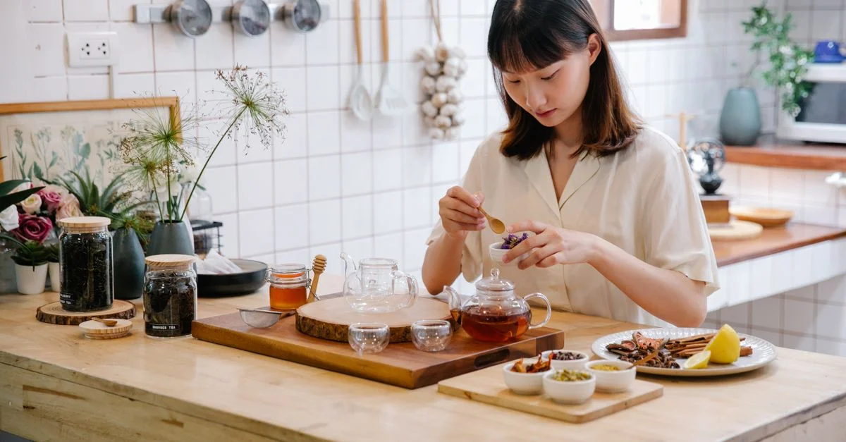 Une jeune femme dans une cuisine moderne préparant du thé aux herbes avec des ingrédients frais. Cadre naturel et apaisant.