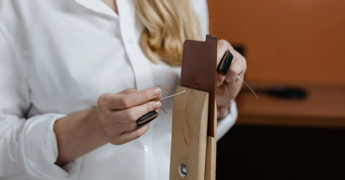 Gros plan sur une couturière cousant du cuir, avec les mains utilisant aiguille et fil.