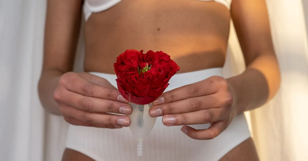 Gros plan sur une femme tenant une coupe menstruelle avec une rose rouge, mettant en avant l'hygiène féminine éco-responsable.