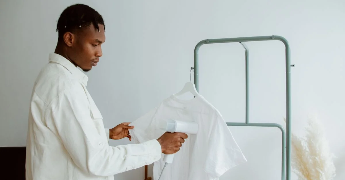 Un homme utilise un steamer pour rafraîchir une chemise blanche sur un porte-vêtements dans un intérieur minimaliste.