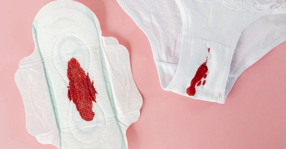 Gros plan sur une string blanche et une serviette hygiénique avec du sang menstruel sur un fond rose.