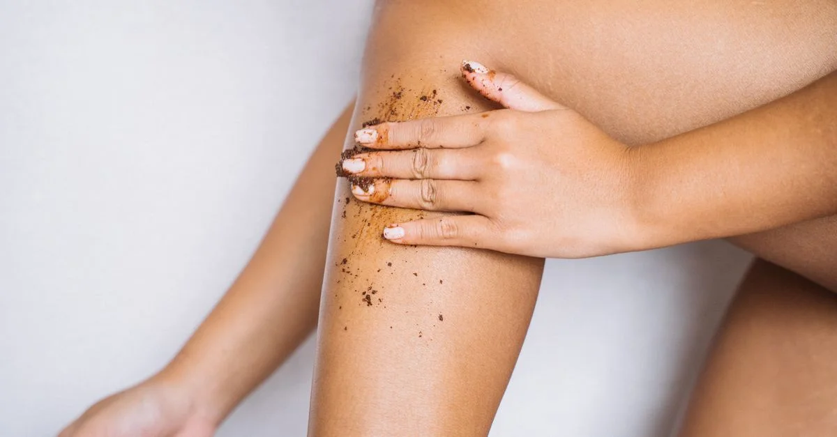 Femme appliquant un gommage exfoliant sur sa jambe pour des soins de la peau lisses.