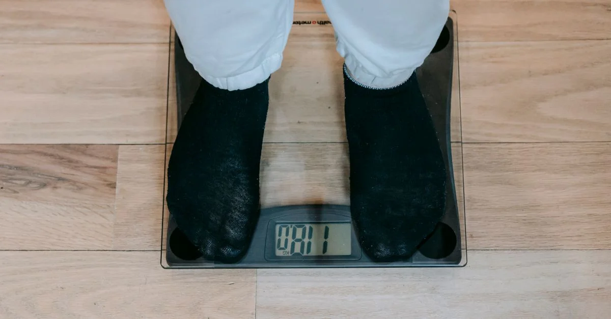 Une personne en chaussettes se tient sur une balance numérique dans une salle de bain, concentrée sur la mesure du poids.