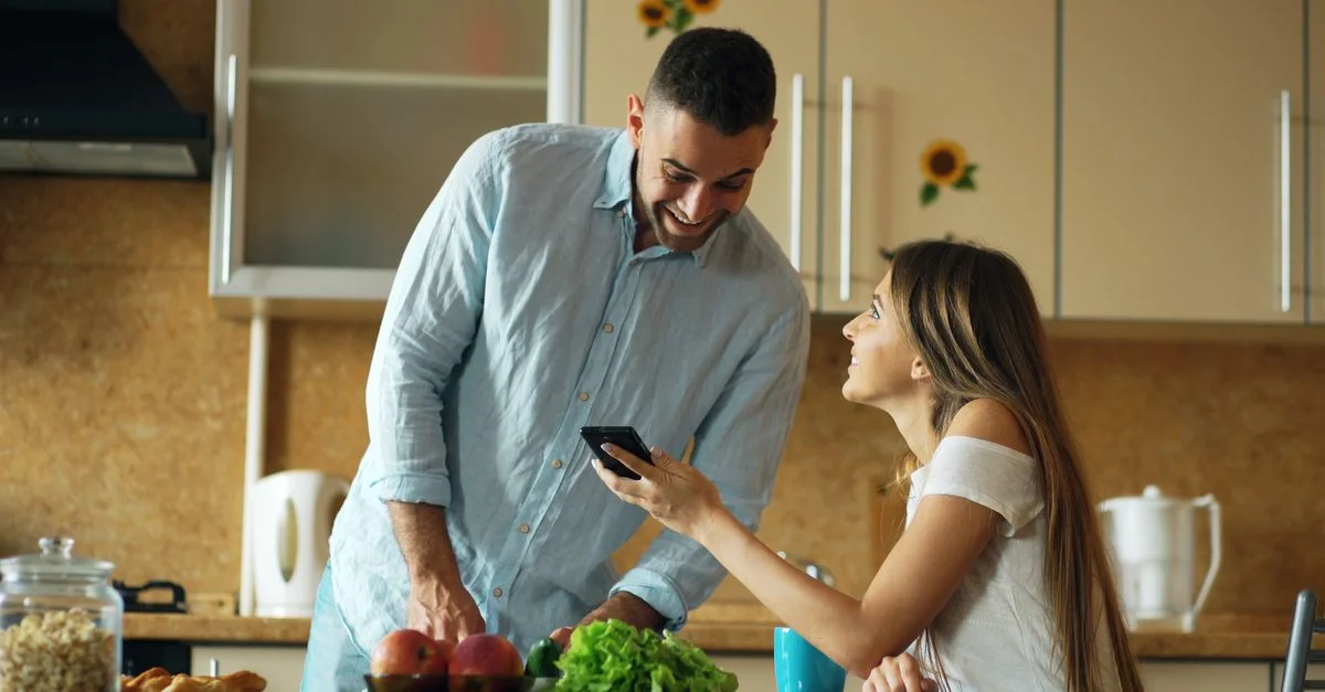 Un couple heureux dans une cuisine lumineuse, partageant des rires et préparant des aliments frais.