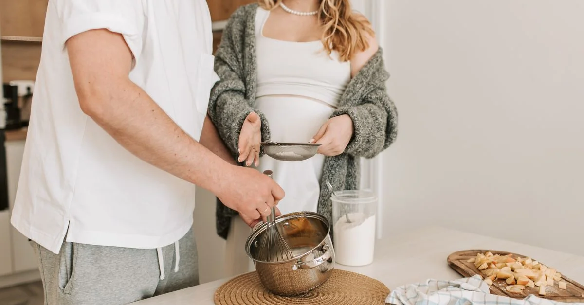 Couple enceinte cuisinant ensemble dans une cuisine chaleureuse, mettant en avant l'amour et l'attention.
