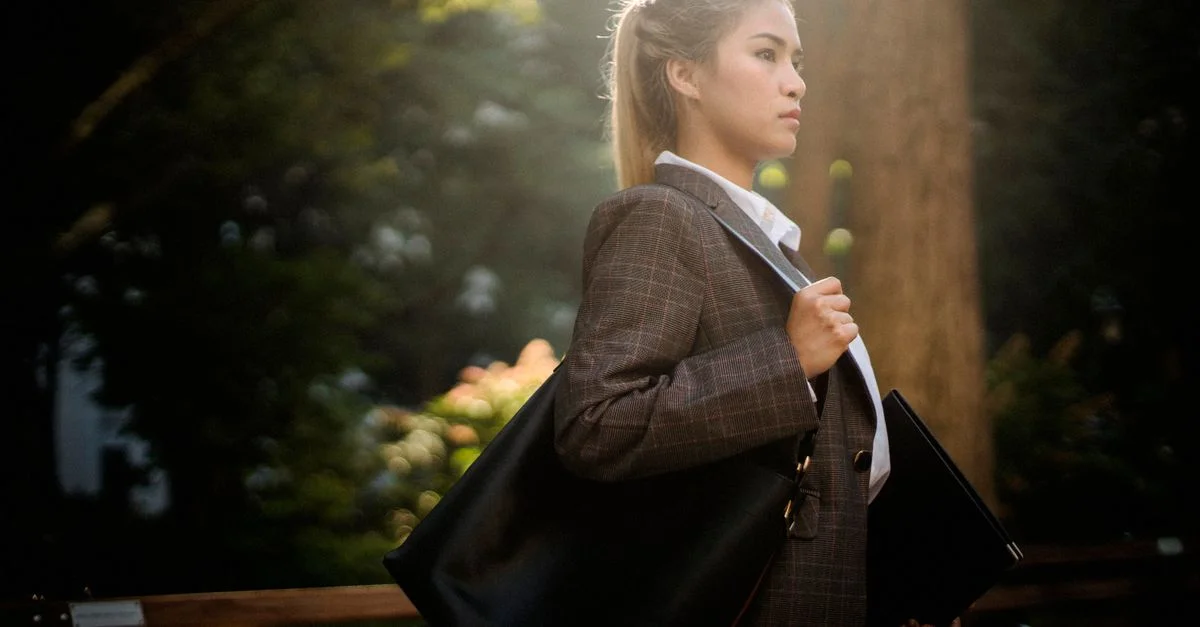 Jeune femme en costume marchant avec confiance à travers un parc baigné de soleil.