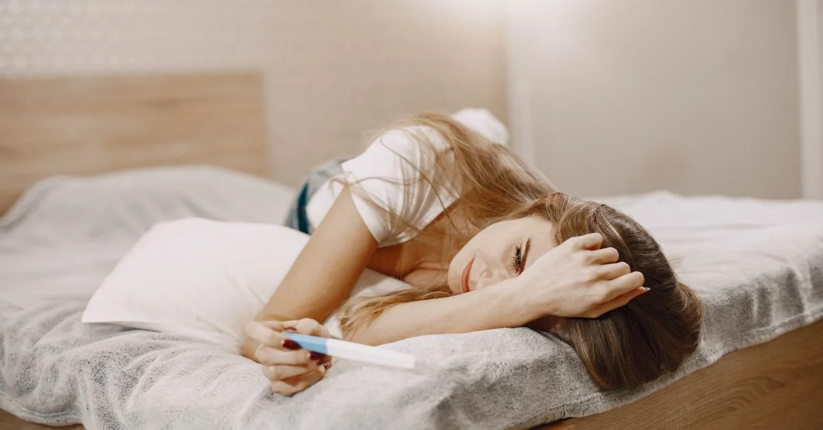 Une femme allongée sur un lit, tenant un test de grossesse, en pleine contemplation.