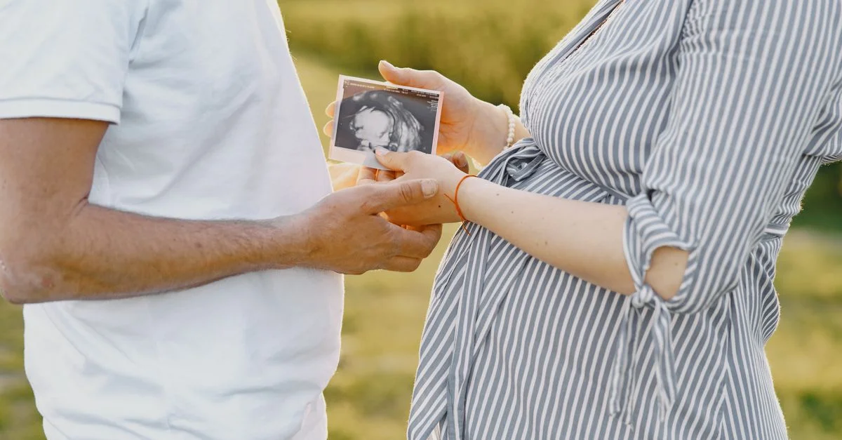 Un couple tient une image d'échographie, représentant la grossesse et l'amour familial, dans un cadre extérieur.