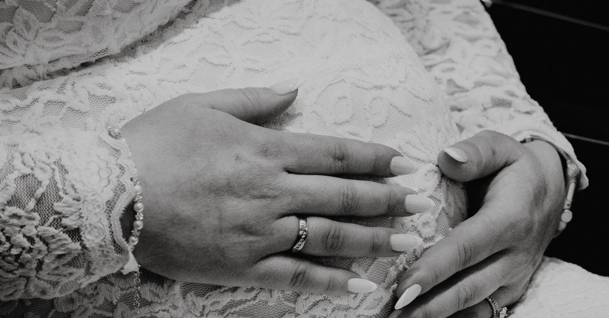 Photo en noir et blanc d'une femme enceinte en dentelle, les mains sur le ventre.