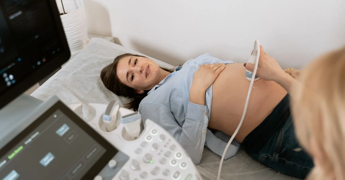 Femme enceinte subissant une échographie, assistée par un professionnel de santé dans une clinique médicale.