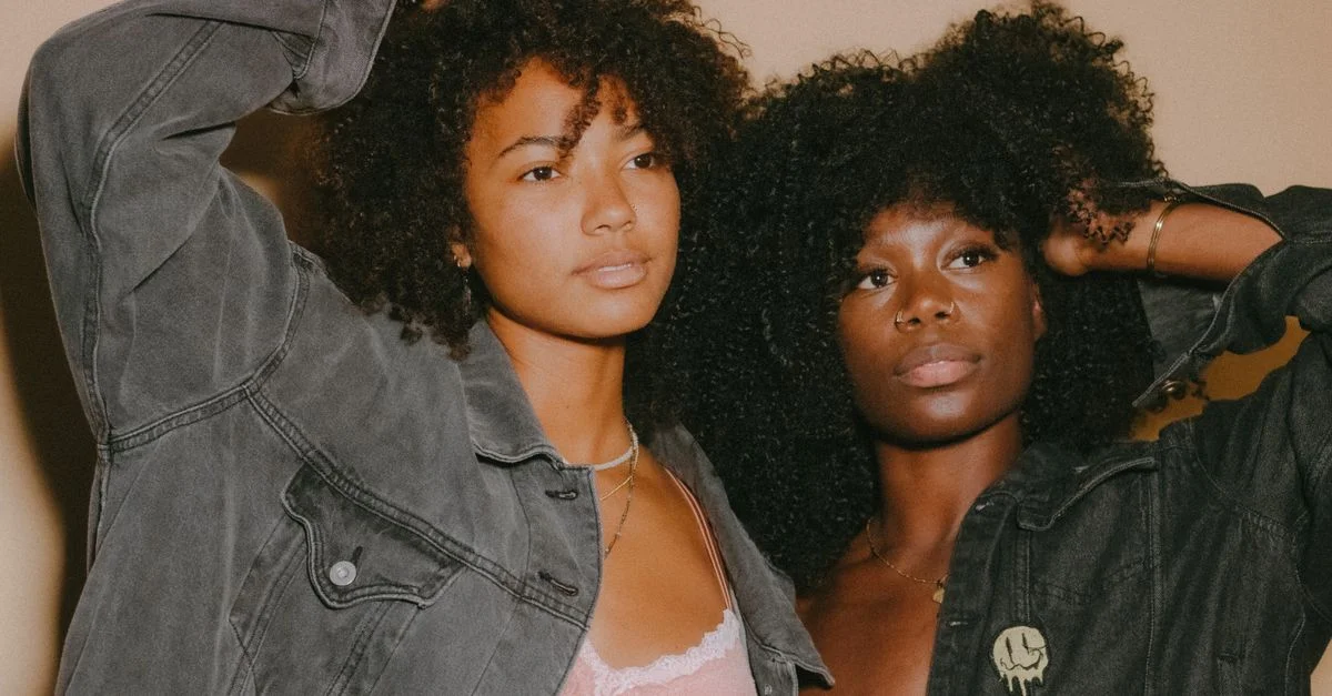 Deux jeunes femmes noires avec des cheveux afro posent avec confiance dans des vestes en denim, mettant en avant la mode moderne.
