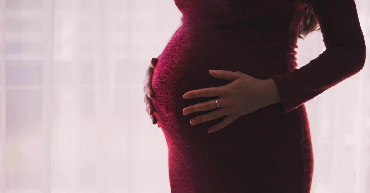 Silhouette d'une femme enceinte tenant doucement son ventre, soulignant la maternité et l'anticipation.