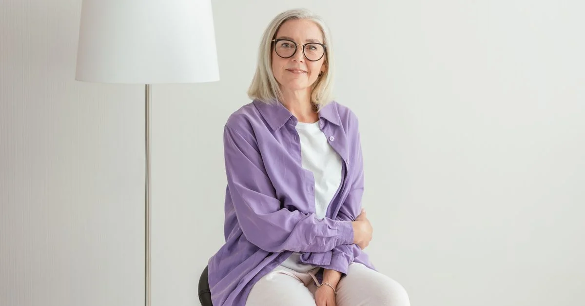 Portrait d'une femme senior heureuse avec des lunettes et des cheveux blancs, portant des vêtements décontractés.