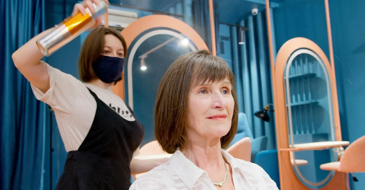 Un coiffeur applique de la laque sur la nouvelle coiffure d'une femme senior dans un salon moderne.