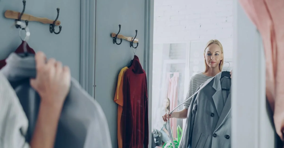 Une femme tenant une veste se reflète dans un miroir de magasin, choisissant sa tenue.