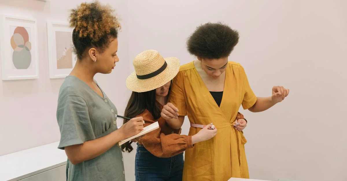 Trois femmes collaborent sur les mesures de robes dans un studio de mode.